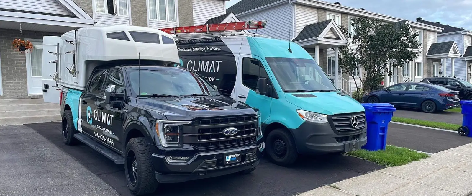 Camion et fourgon de Climat Distinction stationnés dans une entrée, en été